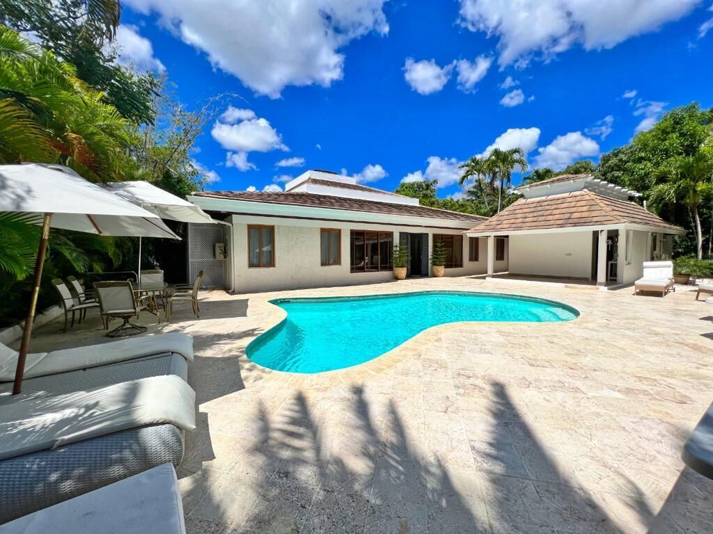 Ett modernt hus med en swimmingpool, utemöbler och en klar, blå himmel.