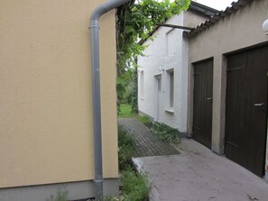 Un estrecho callejón con un muro color beige a la izquierda y un edificio blanco con dos ventanas y una puerta a la derecha.