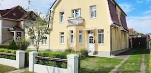 A two-story residential building with a yellow facade, a balcony with a metal railing, and a brick entrance. - Möwe 1 - Holiday apartment Möwe 1 with terrace near the sandy beach in Kühlungsborn (Kühlungsborn)
