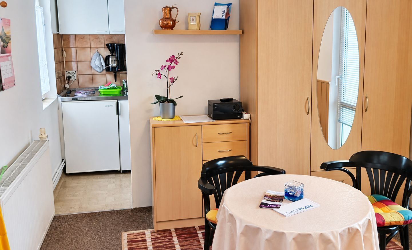 Une cuisine compacte équipée d’une machine à café, d’une orchidée en pot et d’une petite table avec une chaise.