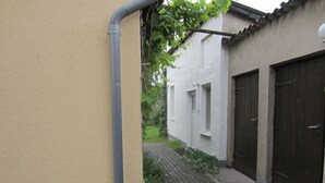 Un estrecho callejón con un muro color beige a la izquierda y un edificio blanco con dos ventanas y una puerta a la derecha.