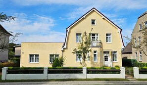 A two-story residential building with a yellow facade, a balcony, and a small garden area. - Möwe 1 - Holiday apartment Möwe 1 with terrace near the sandy beach in Kühlungsborn (Kühlungsborn)