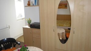 Un dormitorio con un armario de madera, una cama, una mesita con una planta y una silla.