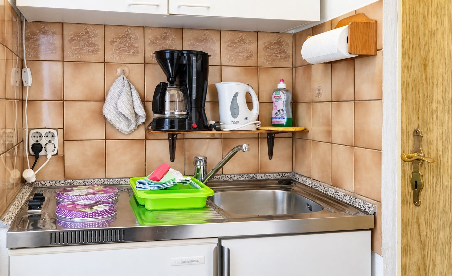 Una cocina con cafetera, hervidor y escurreplatos.