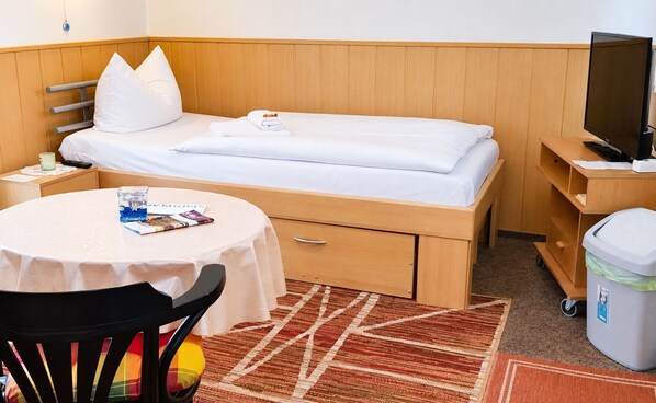 A hotel room with a single bed, a small table with a chair, a television, and a trash bin. - Möwe 1 - Holiday apartment Möwe 1 with terrace near the sandy beach in Kühlungsborn (Kühlungsborn)