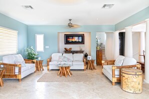 Una sala de estar con un sofá blanco, dos sillones, una mesa de centro y un televisor montado en la pared.