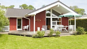 En röd byggnad med en täckt uteplats, vita utemöbler och ett grönt parasoll.