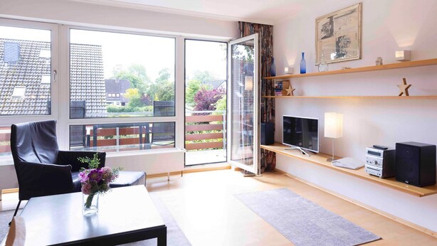 Un salon moderne doté d’une porte vitrée donnant sur un balcon, d’un téléviseur à écran plat, d’un système audio et d’une bibliothèque.