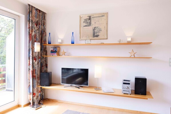 A modern living room with a flat-screen TV, two speakers, and a bookshelf with decorative items.