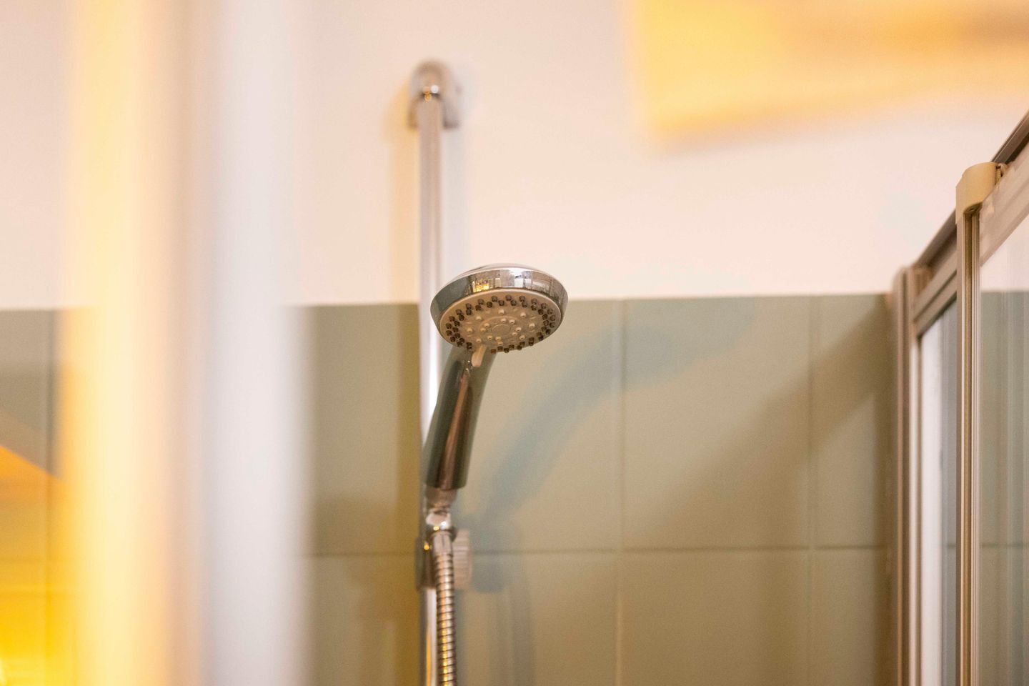 A showerhead in a bathroom with tiled walls.