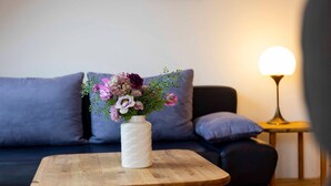 A wooden table with a white vase of flowers in front of a dark sofa.