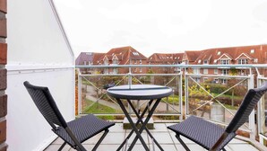 A balcony with a table and two chairs, overlooking a residential area with houses and a garden.