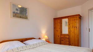 A bedroom with a bed, a wooden wardrobe, a nightstand with a lamp, and a framed picture on the wall.