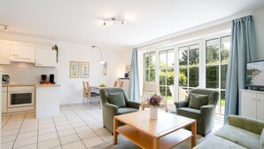 A modern living room with a dining area, kitchen, and large windows offering a view of greenery. - (OST1) Holiday apartment "Lörper 1" - Holiday apartment "Lörper 1" up to 3 persons (Timmendorfer Strand)