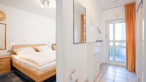 A hotel room with a bed, bedside table, lamp, mirror, wardrobe, and a bathroom with a shower and toilet. - (OST1) Holiday apartment "Lörper 1" - Holiday apartment "Lörper 1" up to 3 persons (Timmendorfer Strand)