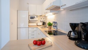 A modern kitchen with white cabinets, a microwave, a toaster, a coffee maker, and a cutting board with tomatoes. - (OST1) Holiday apartment "Lörper 1" - Holiday apartment "Lörper 1" up to 3 persons (Timmendorfer Strand)