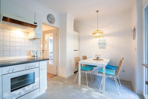 Une cuisine compacte dotée d’une cuisinière moderne, d’un coin repas avec une table blanche et des chaises bleues, et d’un luminaire suspendu.