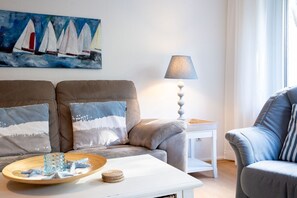 A living room with a sofa, a side table, a lamp, and a painting of sailboats.