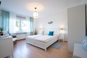 A bedroom with a double bed, bedside tables with lamps, a window with curtains, a radiator, and a wall decoration. - (MEI71) Apartment "Strandlust" - Apartment "Strandlust" up to 4 persons (Timmendorfer Strand)