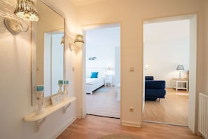 A hallway leading to a bedroom with a bed, bedside table, lamp, and a blue sofa. - (MEI71) Apartment "Strandlust" - Apartment "Strandlust" up to 4 persons (Timmendorfer Strand)
