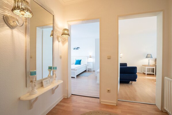 A hallway leading to a bedroom with a bed, bedside table, lamp, and a blue sofa.
