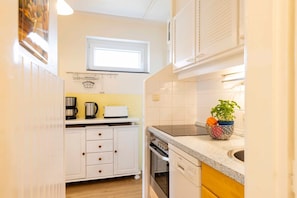 A compact kitchen with white cabinets, a built-in oven, a dishwasher, and a window above the sink.