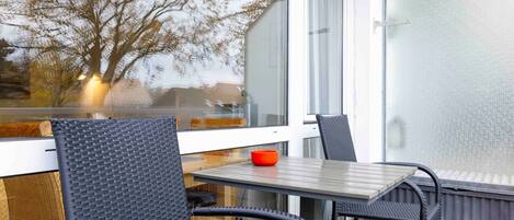 A balcony with wicker chairs and a table, overlooking a tree and a building.