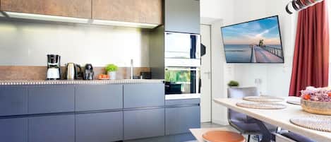 A modern kitchen with grey cabinets, a built-in oven, and a dining area with a table and chairs.