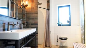 A bathroom with a white sink, black faucets, a shower curtain, a toilet, and a window with a view.