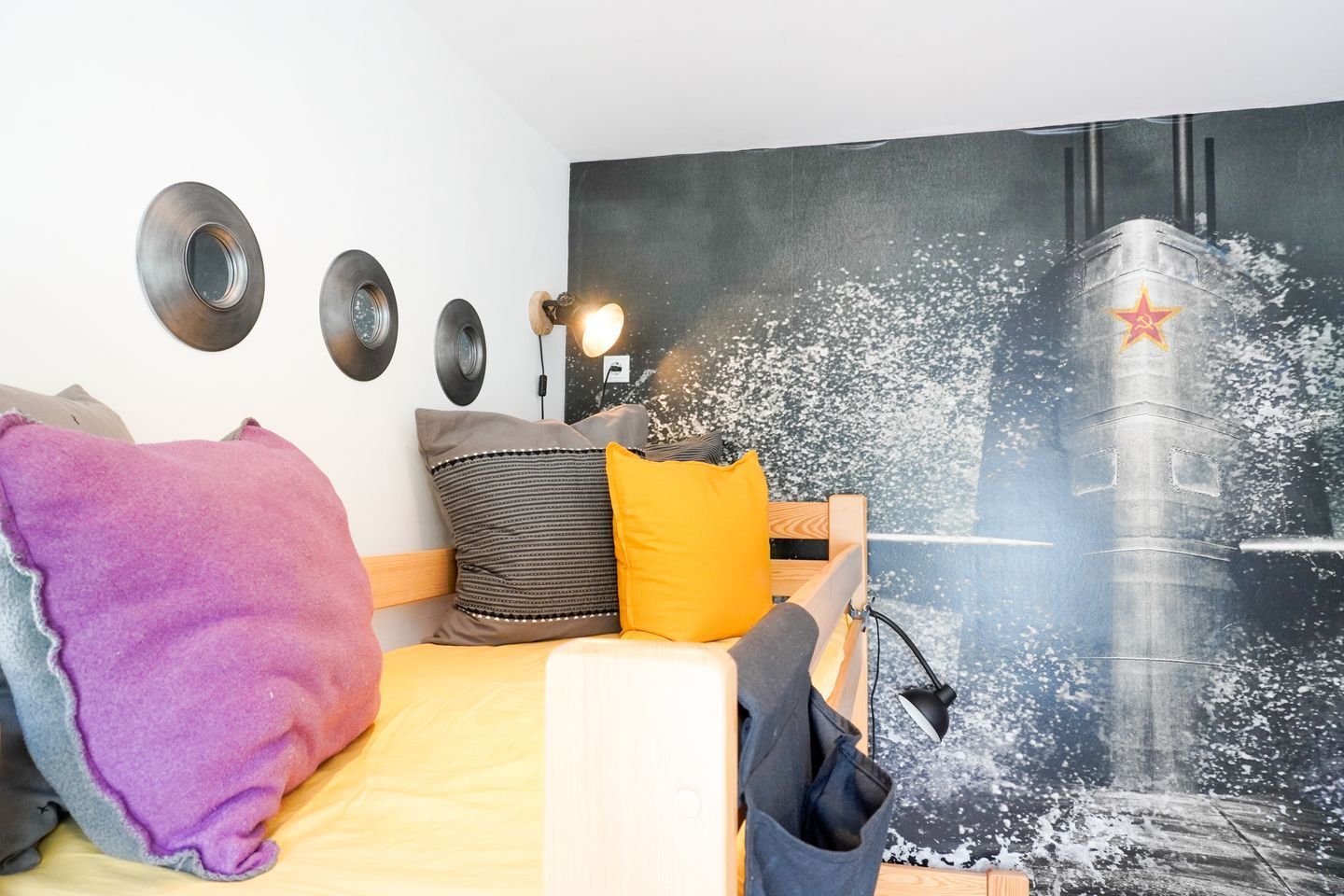 Ein Bett mit Kissen, eine Wandlampe und ein großes Poster eines Gebäudes mit einem Stern.