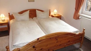 Uma cama de casal com estrutura de madeira, duas mesas de cabeceira com abajures e uma janela com cortinas.