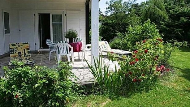 Um alpendre coberto com área de estar externa, um caminho de pedra e um jardim com flores vermelhas.