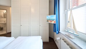 A bedroom with a bed, a wardrobe, a television, and a window with a sailboat model. - (OST35c) Holiday apartment "Sonnendeck" - Holiday apartment "Sonnendeck" for 2 persons (Timmendorfer Strand)