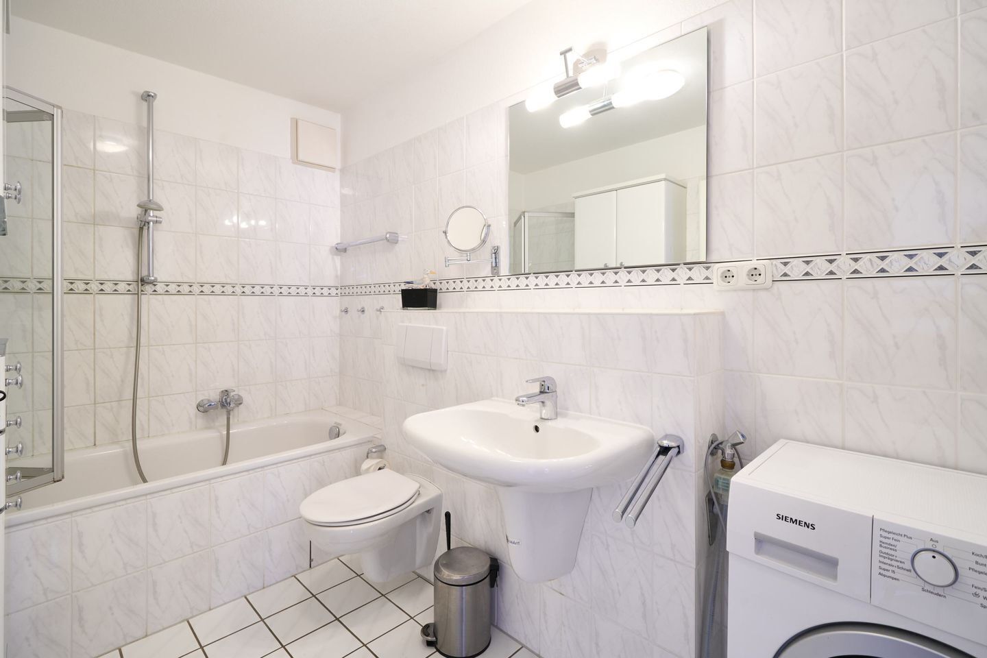 A bathroom with a bathtub, toilet, sink, and a Siemens washing machine.