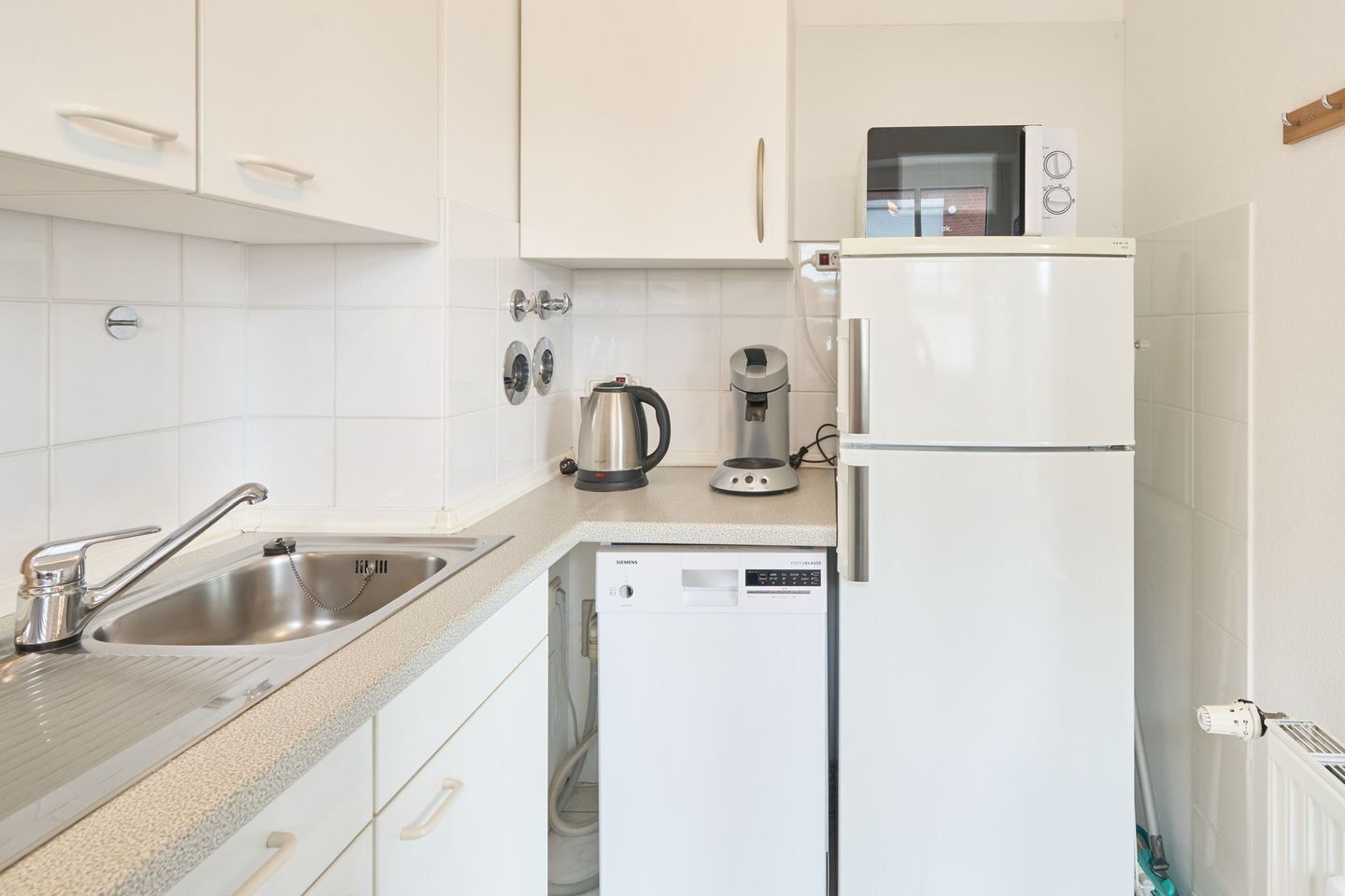 A modern kitchen with white cabinets, a stainless steel sink, a coffee maker, a kettle, and a built-in microwave.