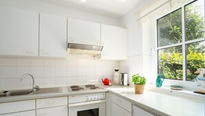 Una cocina moderna con gabinetes blancos, un lavamanos de acero inoxidable, un horno empotrado y una ventana con vistas al verdor.
