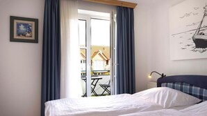 A bedroom with two beds, a view of a balcony with a table and chairs, and a painting of a ship on the wall. - (OST29) Apartment "Komoran" - Apartment "Komoran" for 2 persons (Timmendorfer Strand)