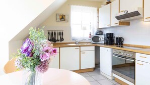 A kitchen with white cabinets, a wooden countertop, a microwave, a coffee maker, and a vase with flowers on a table. - (OST29) Apartment "Komoran" - Apartment "Komoran" for 2 persons (Timmendorfer Strand)