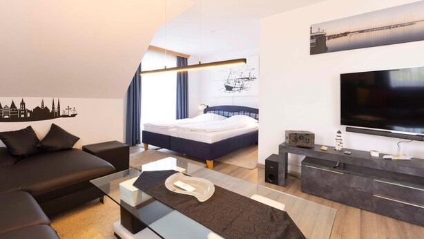 A modern hotel room with a bed, a sofa, a TV, and a city skyline decal on the wall. - (OST29) Apartment "Komoran" - Apartment "Komoran" for 2 persons (Timmendorfer Strand)