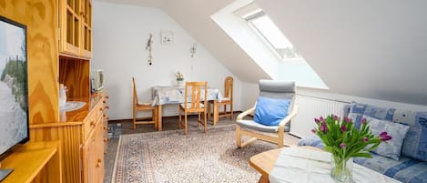 A cozy attic room with a sloped ceiling, wooden furniture, a dining table, and a skylight.