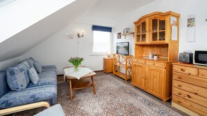 A cozy attic bedroom with a sloped ceiling, a wooden cabinet with glass doors, a small dining table, and a blue patterned sofa.