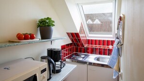 A kitchen with a window, red tiles, a plant, and a kettle. - (HER14b) Holiday apartment "Hartig 2" - Holiday apartment "Hartig 2" up to 2 persons (Timmendorfer Strand)