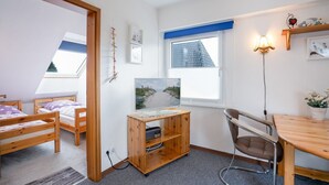A room with bunk beds, a desk with a computer, a chair, a window with a view of a building, and a wall-mounted shelf with decorative items. - (HER14b) Holiday apartment "Hartig 2" - Holiday apartment "Hartig 2" up to 2 persons (Timmendorfer Strand)