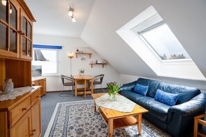 A cozy loft apartment with a dining area, a sofa, a wooden cabinet, and a skylight.