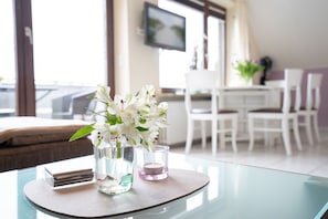 Une chambre d’hôtel moderne avec une table en verre, un vase de fleurs blanches et une petite bougie.