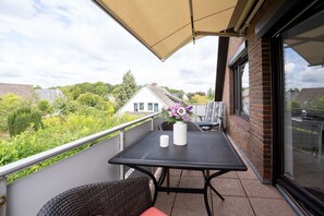 Un balcon avec une table et des chaises, un pot de fleurs et une vue sur les maisons et la végétation environnantes.