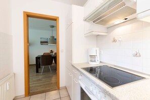 Una cocina moderna con placa de inducción, cafetera y zona de comedor con mesa y sillas.