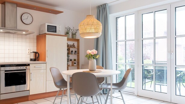A modern kitchen with a dining area, featuring a round table, grey chairs, a hanging light fixture, and a view of the outdoors through large windows. - (OST8) Holiday apartment "Lörper 2" - Holiday apartment "Lörper 2" up to 4 persons (Timmendorfer Strand)