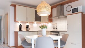 A modern kitchen with white cabinets, a round dining table with two chairs, a coffee maker, and a clock on the wall. - (OST8) Holiday apartment "Lörper 2" - Holiday apartment "Lörper 2" up to 4 persons (Timmendorfer Strand)