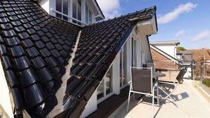 Ein Haus mit einem steilen Dach, einem Balkon mit einem Stuhl und einem klaren Himmel.